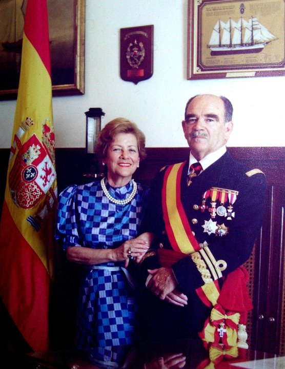 Tomás Gómez Arroyo y su esposa María Victoria «Vivi» Soutullo, juntos y de la mano. Él viste uniforme de gala con banda y condecoraciones; detrás, la bandera de España. Fotografía familiar; fecha y ocasión por confirmar.